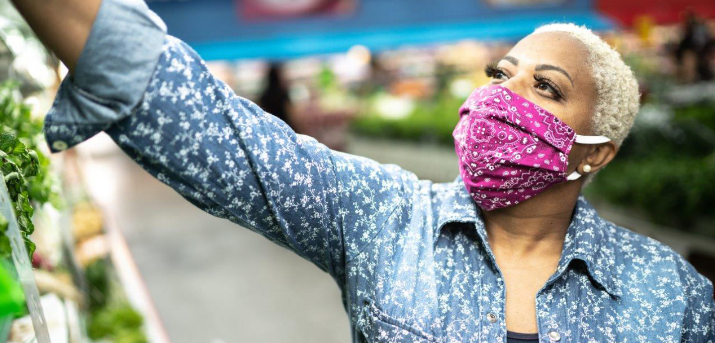 woman in grocery store wearing mask and standing around vegetables