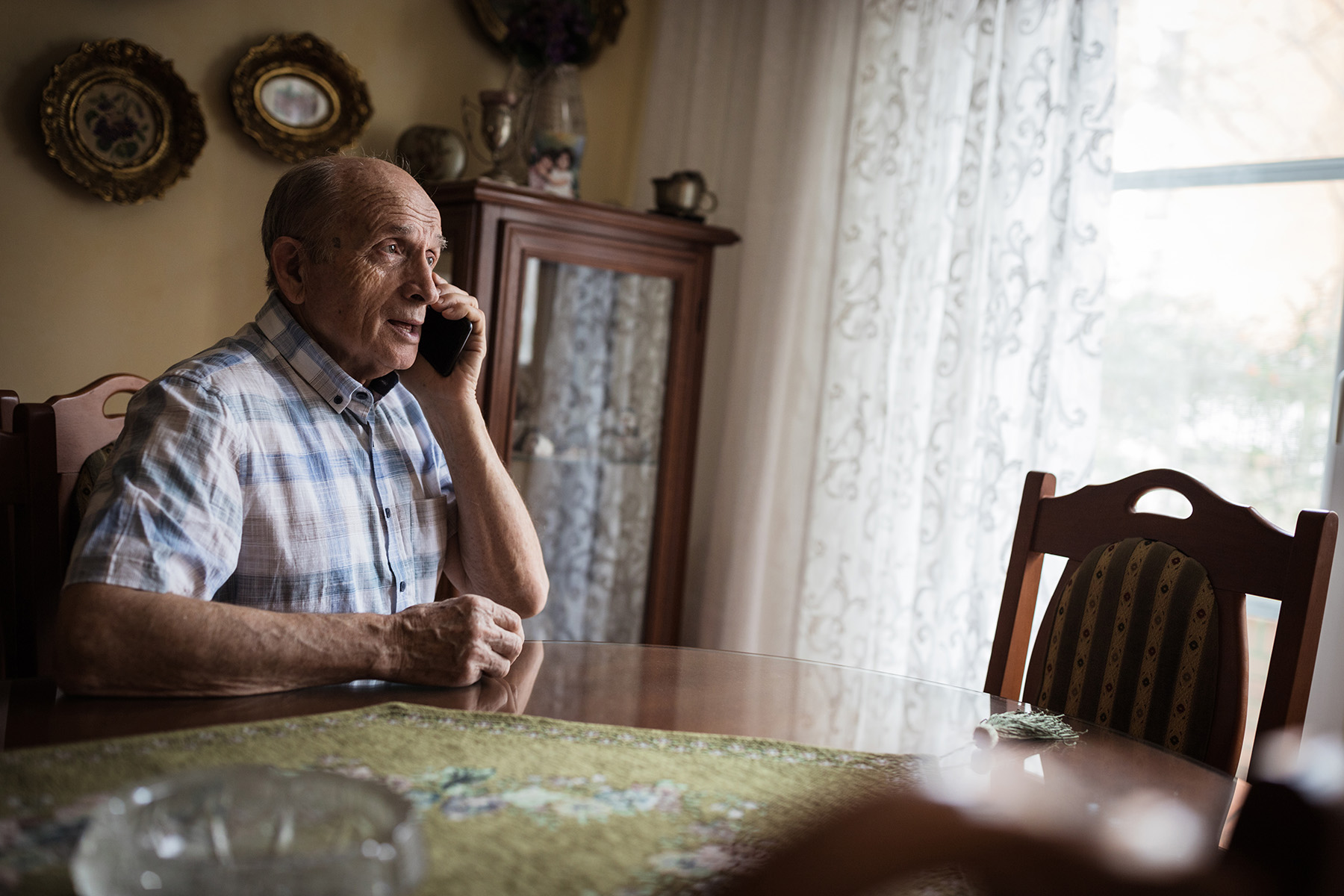 Cheerful senior man using mobile phone at home and sitting at wooden table