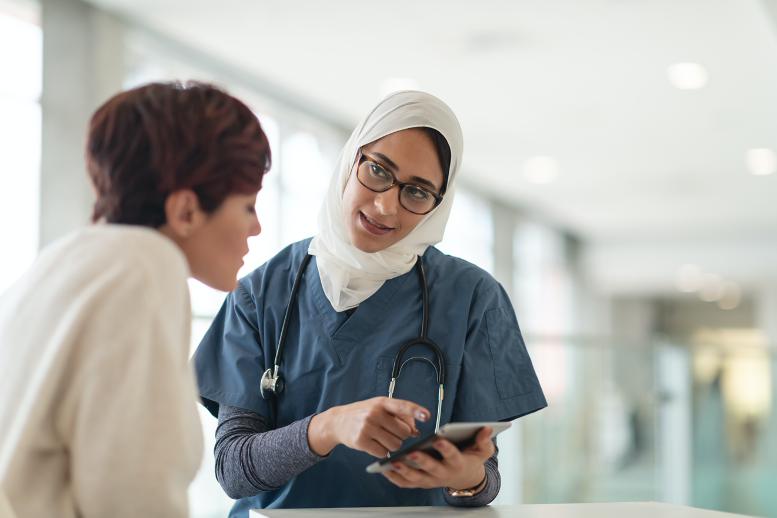 Doctor in blue scrubs reading off of tablet while speaking to patient