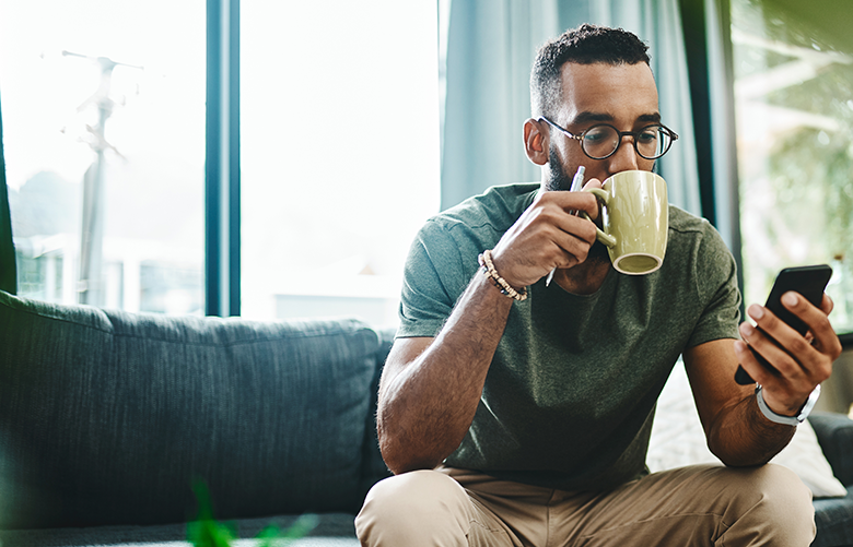 man drinking coffee sitting on couch looking at phone