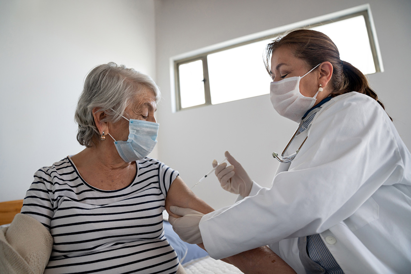 Latin American senior woman getting a COVID-19 vaccine by a doctor at a nursing home