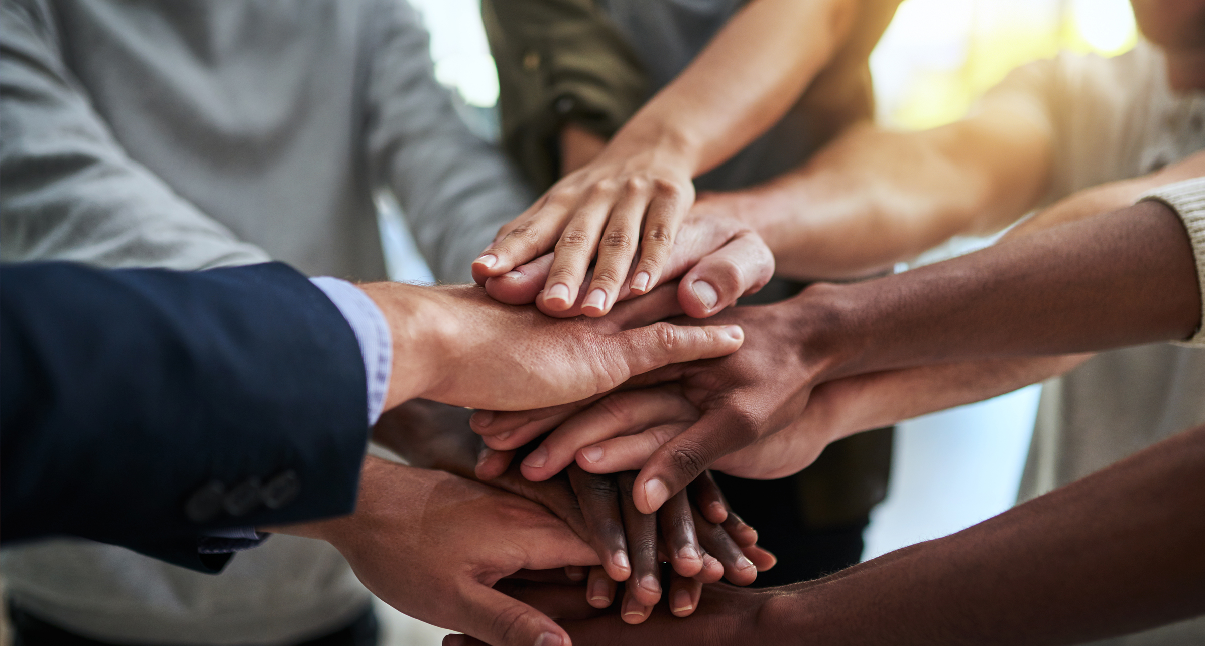 hands of a wide variety of skin colors stacking on top of one another to indicate teamwork